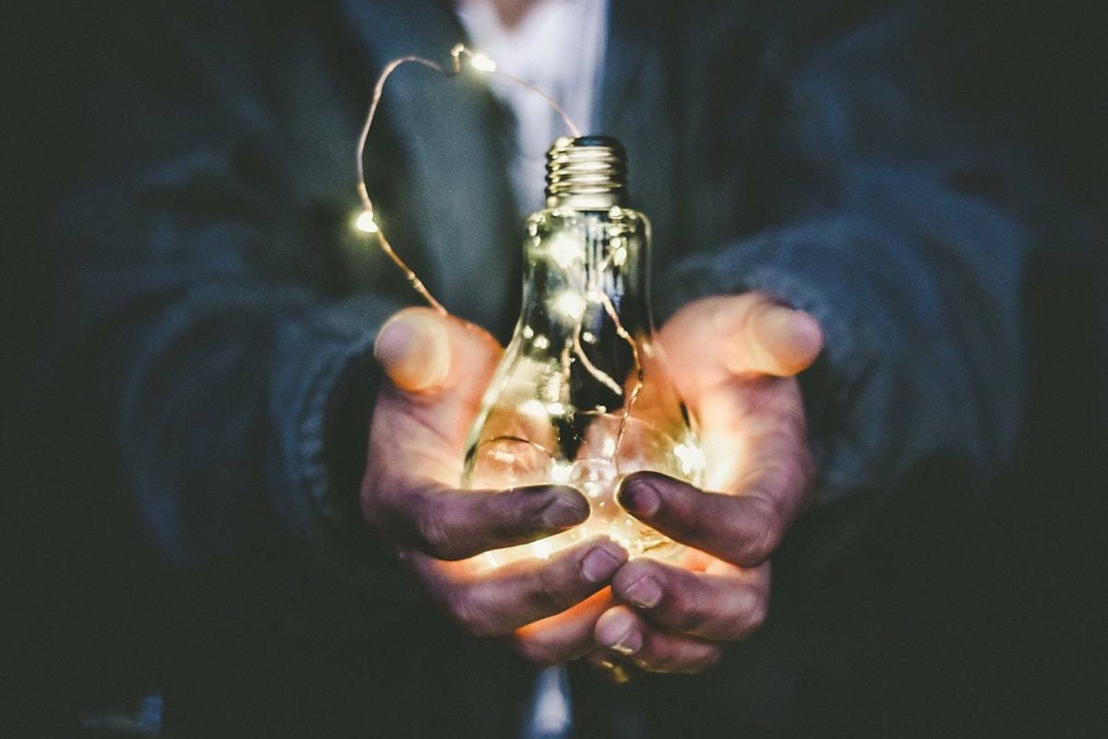 A glowing light bulb held in cupped hands.